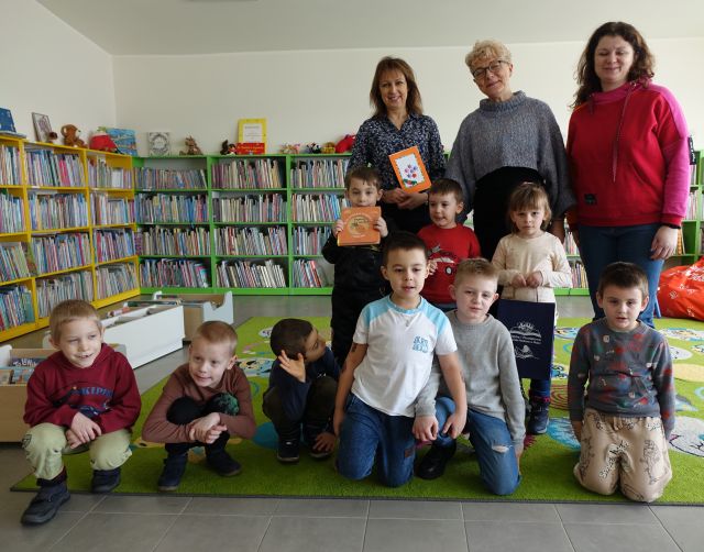 przedszkolaki, dwie przedszkolanki i dyrektorka biblioteki pozują do zdjęcia, w tle regały z książkami