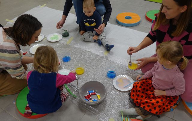 dzieci i rodzice bawią się płynem z barwnikami na papierowych talerzykach