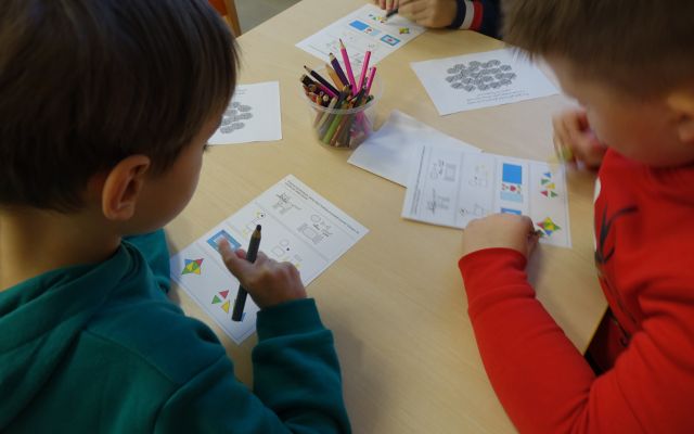 trzech chłopców rozwiązuje zagadki na kartkach