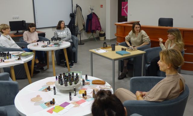 uczestnicy warsztatów olejkowych siedzą na siwych fotelach przy białych okrągłych stołach z olejkami