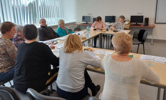 seniorzy siedząc przy stolikach uczą się