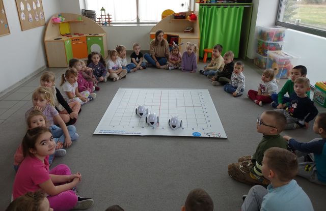 roboty Photon na macie w przedszkolu, wokół nich siedzi grupa przedszkolna i pani przedszkolanka