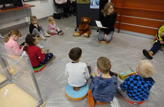 bibliotekarka czyta siedzącym na pufach dzieciom