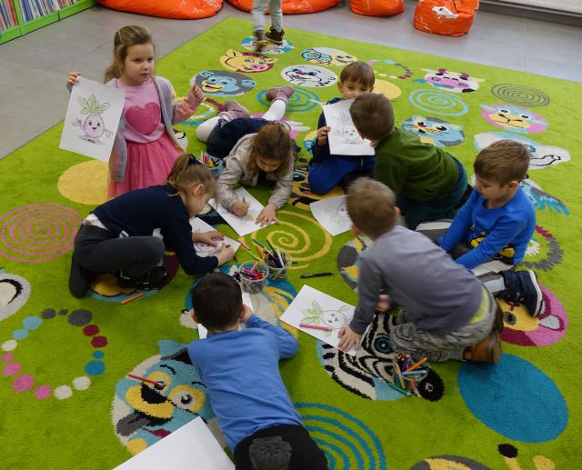przedszkolaki leżą na kolorowym dywanie i malują na kartkach
