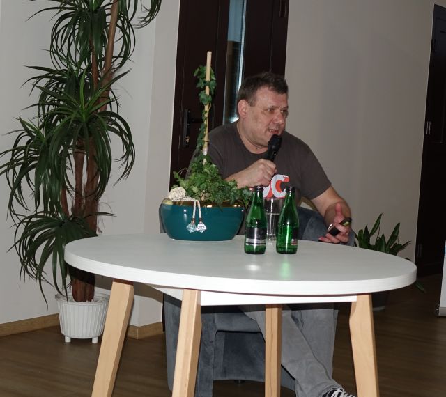 mężczyzna siedzi z mikrofonem przy białym stole