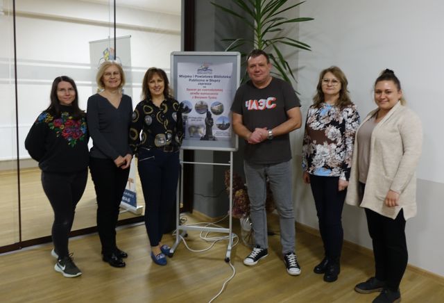 pracownice biblioteki pozują do zdjęcia z autorem na tle plakatu zapraszającego na spotkanie