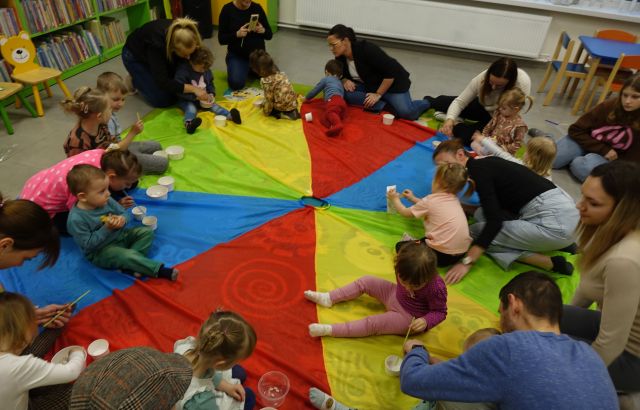 dzieci i rodzice siedzą na kolorowej chuście animacyjnej