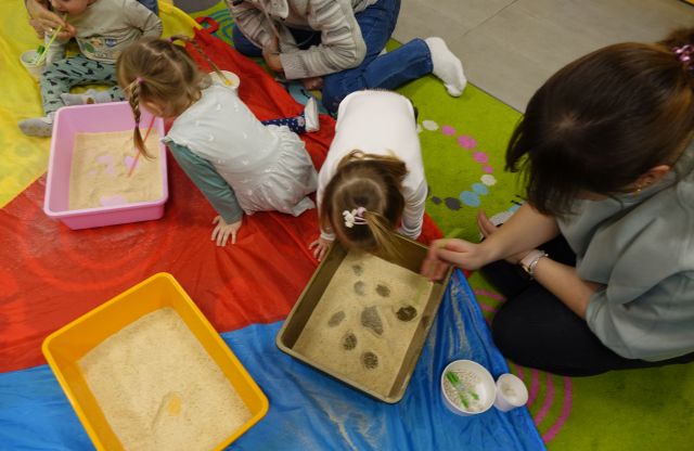 małe dzieci pod opieką rodziców dmuchają rurkami w piasek