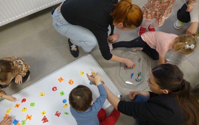 małe dzieci pod opieką rodziców układają literki