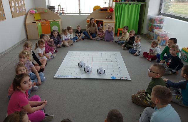 dzieci siedzą na podłodze w okręgu, przed nimi 3 roboty Photon