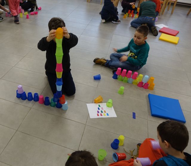 dzieci układają jak najwyżej kolorowe kubeczki