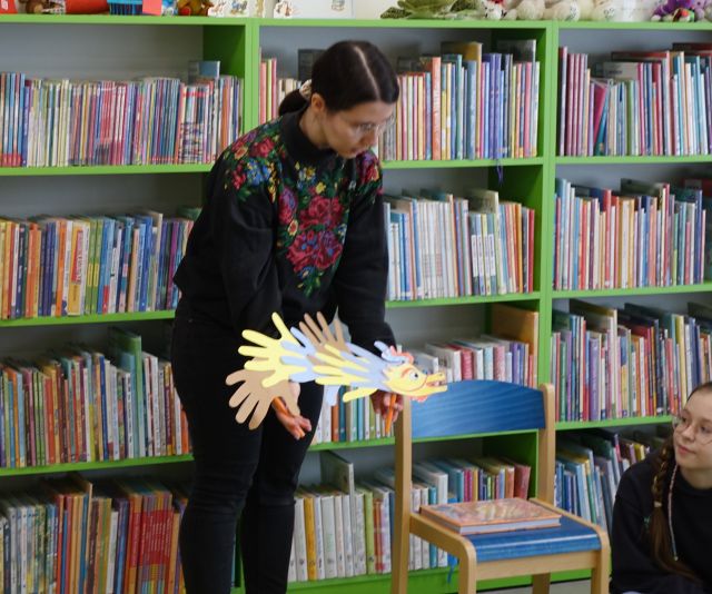bibliotekarka pokazuje dzieciom smoka z papieru, w tle regały z książkami