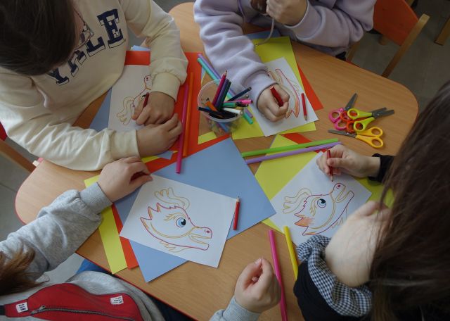 dzieci siedząc przy stolikach rysują smoki
