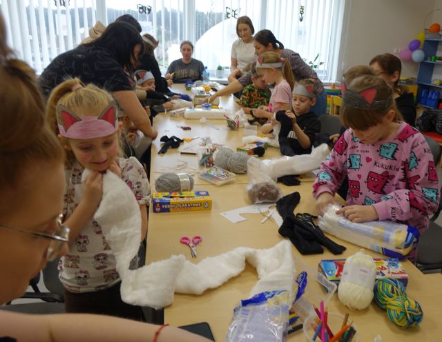 dzieci uczestniczące w warsztatach siedzą przy stołach na których leżą różne artykuły (papier, nici, wełna, materiały)