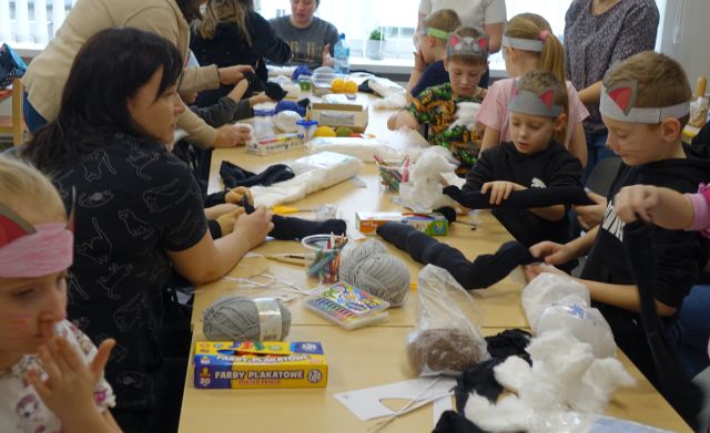 dzieci uczestniczące w warsztatach siedzą przy stołach na których leżą różne artykuły (papier, nici, wełna, materiały)