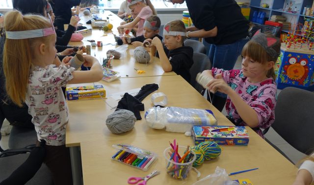 dzieci uczestniczące w warsztatach siedzą przy stołach na których leżą różne artykuły (papier, nici, wełna, materiały)