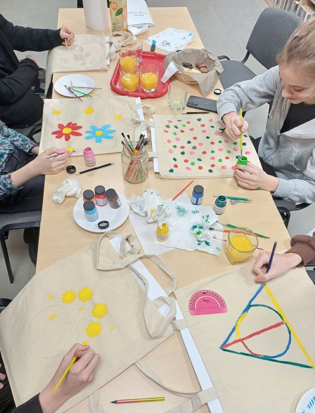 młodzież siedząca przy stołach maluje torby