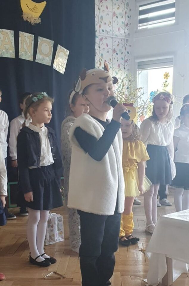chłopiec z mikrofonem w stroju baranka, za nim stoją przedszkolaki