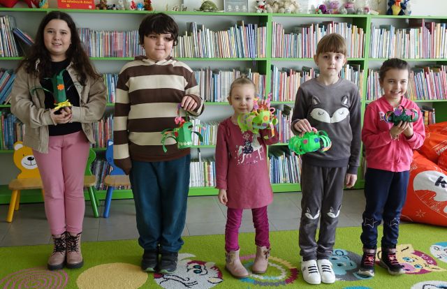 5 dzieci pozuje do zdjęcia pokazując wykonane przez siebie kwiatki, w tle regały z książkami