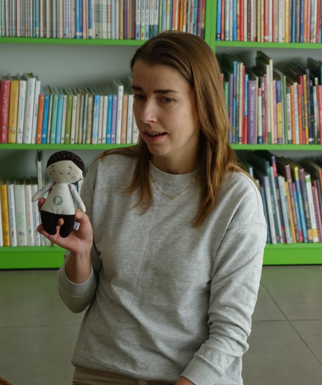kobieta pokazuje maskotkę Pucia, w tle regały z książkami