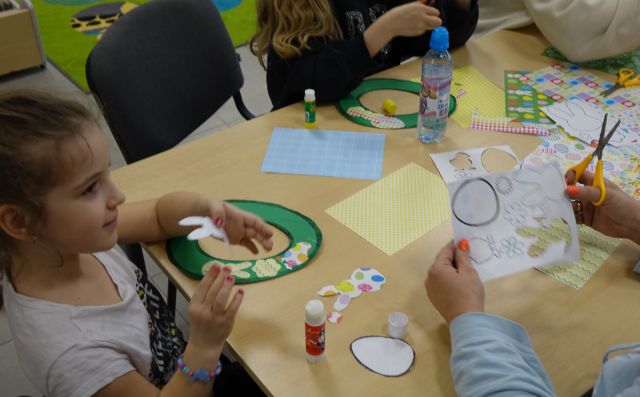 dzieci naklejają na wycięte z zielonych kartek obręcze kwiatki, króliczki i jajka wycięte z papieru