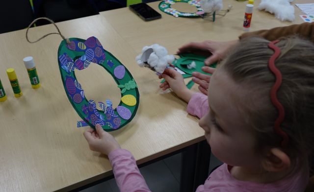 dziewczynka prezentuje wykonany przez siebie wielkanocny wieniec ozdobiony wyciętymi z kartek kwiatami, krliczkami, jajkami