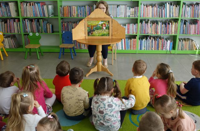 bibliotekarka pokazuje dzieciom Baśn o Czerwonym Kapturku w formie teatrzyku Kamishibai