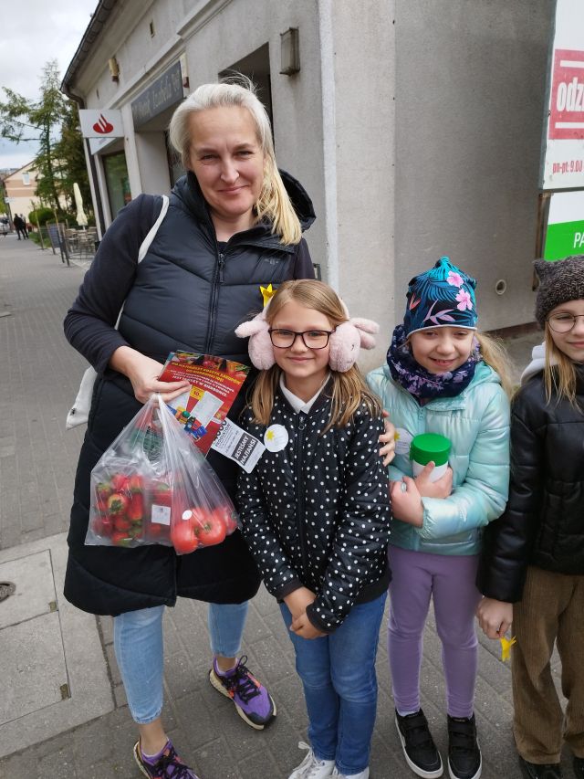 dzieci pozują do zdjęcia z kobietą i przypiętymi żółtymi papierowymi żonkilami