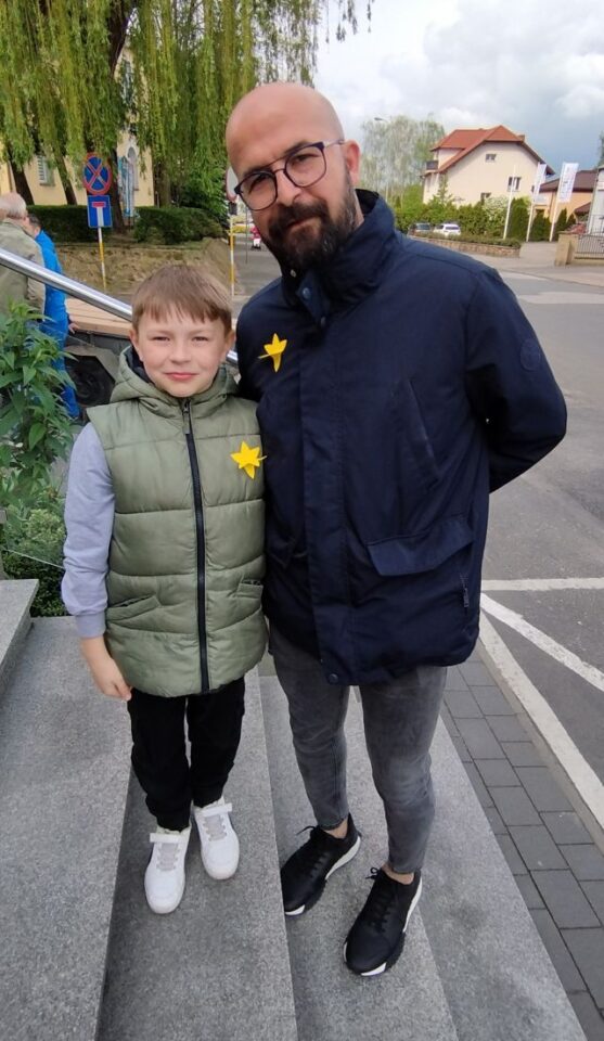 chłopiec pozuje do zdjęcia z mężczyzną, oboje mają przyklejone do kurtek żółte papierowe żonkile