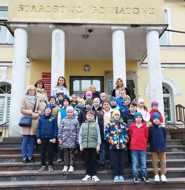 dzieci i 5 osób dorosłych pozuje do zdjęcia na schodach przed wejściem do Starostwa Powiatowego