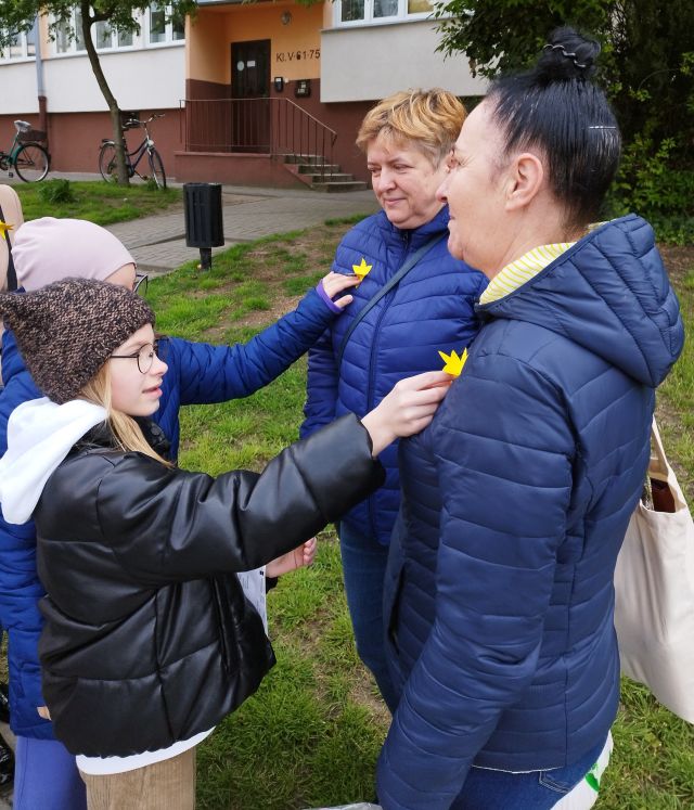 dwie dziewczynki przyklejają dwóm kobietom żółte papierowe żonkile