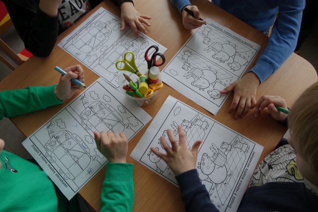 4 dzieci siedzących przy stoliku koloruje postacie z bajek