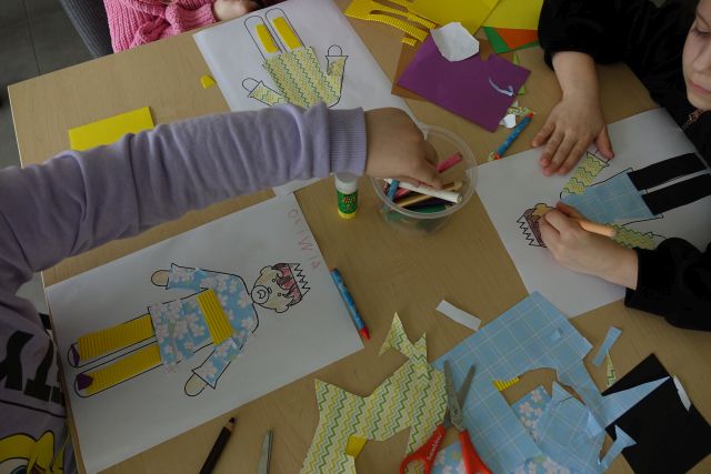 dzieci naklejają kolorowe materiały na naszkicowane na kartkach postacie cesarza