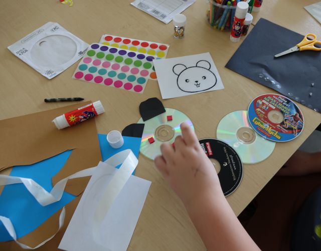 dzięcięca dłoń wykleja na płycie CD kolorowymi karteczkami misia