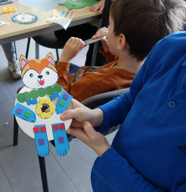 chłopiec pokazuje wykonanego przez siebie misia wyklejonego kolorowymi karteczkami na płycie CD