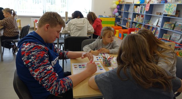 młodzież siedząca przy stolikach koloruje kółka na kartkach