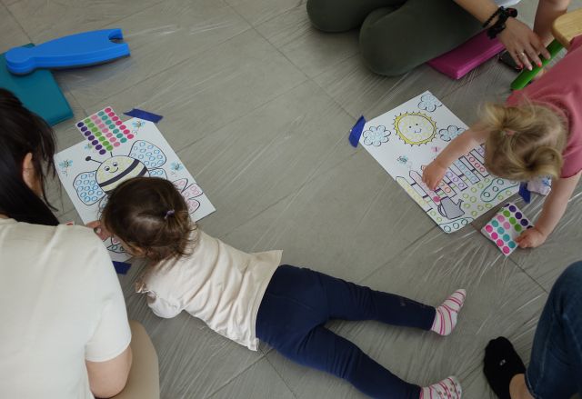 dziewczynka nakleja kółeczka na kartkę z ilustracją kury