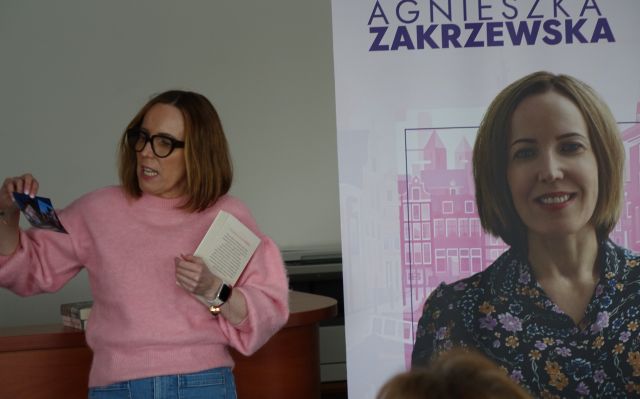 kobieta trzymająca w dłoniach książki, z prawej strony baner z jej zdjęciem