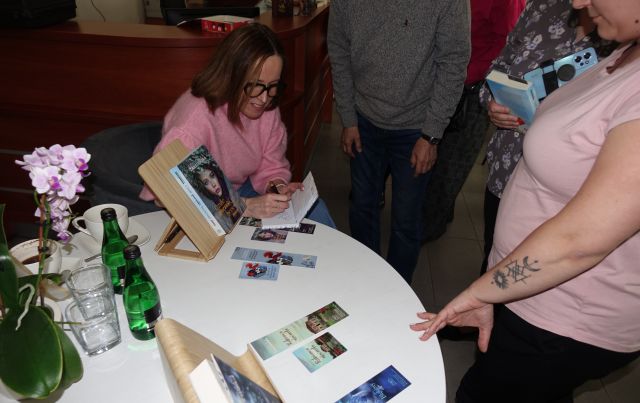 autorka siedząc przy stoliku z książkami podpisuje swoje książki