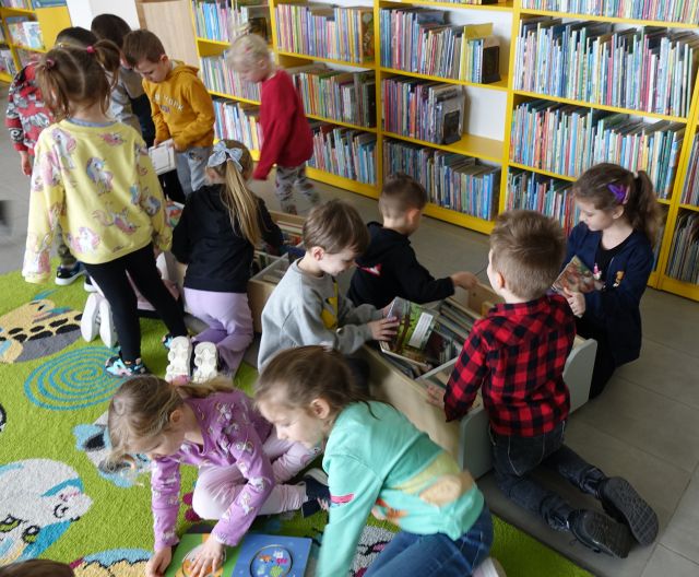 przedszkolaki przeglądaja książki w boxach, w tle regały z książkami