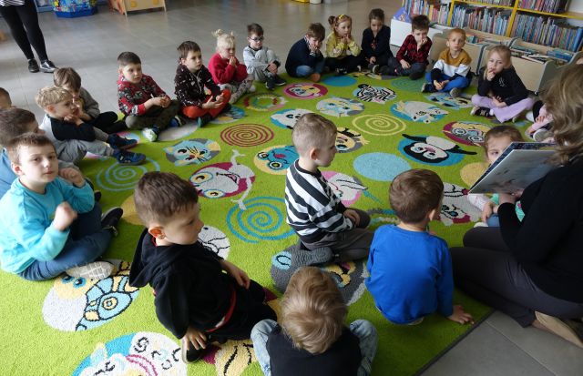 bibliotekarka czyta siedzącym na kolorowym dywanie przedszkolakom książkę