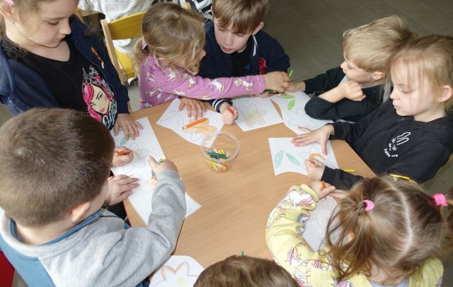 dzieci kolorują siedząc przy stołach żonkile