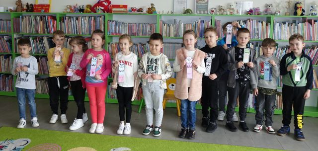 dzieci pozujące do zdjęcia z zakładkami, w tle regały z książkami