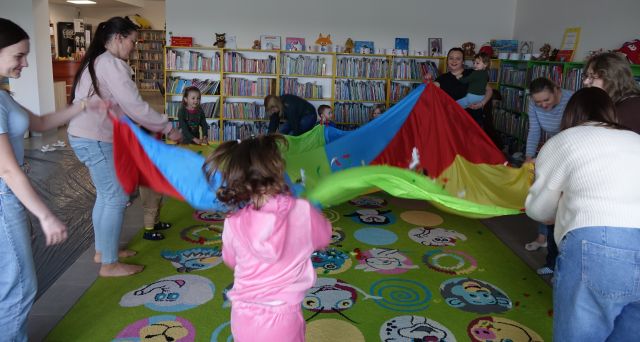 rodzice i dzieci machają kolorową chustą znimacyjną