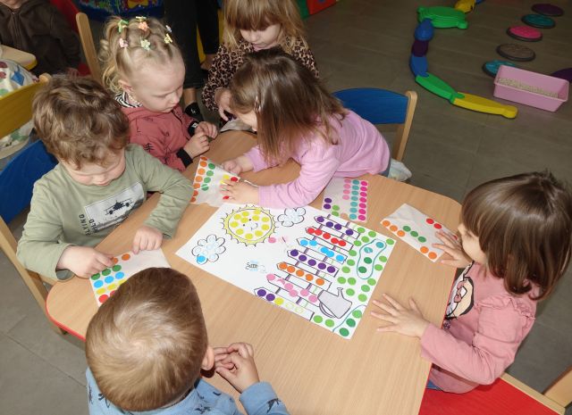 dzieci naklejają kolorowe kółka na kartki z ilustracjami bajkowych postaci