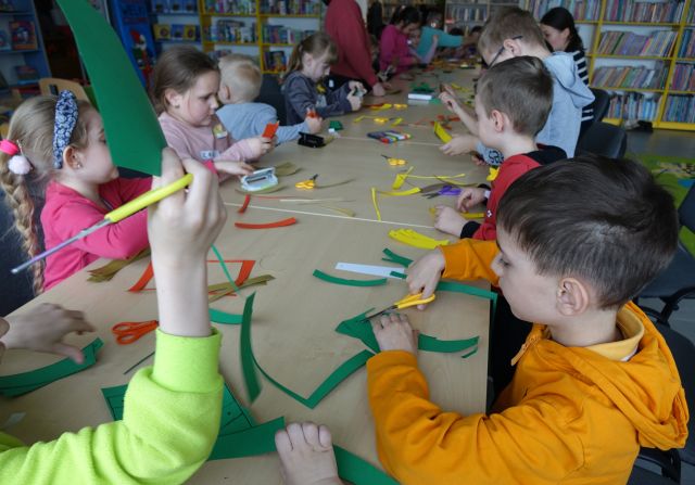 dzieci siedzą przy stołach i wycinają paski z kolorowego papieru