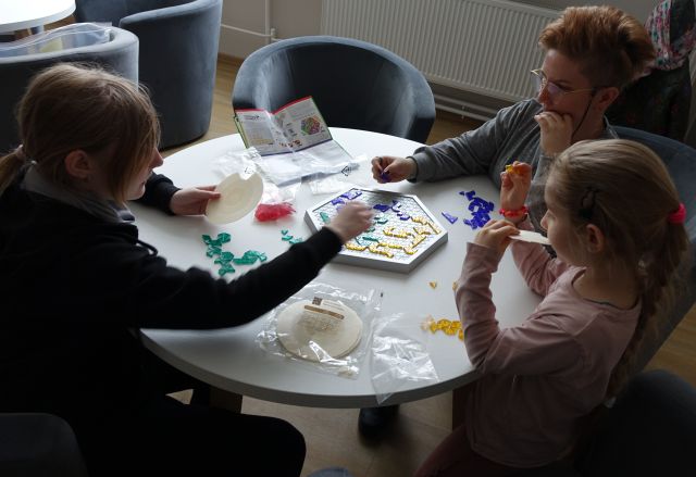 kobieta i dwie dziwczynki grają w grę planszową siedząc przy okrągłym białym stole