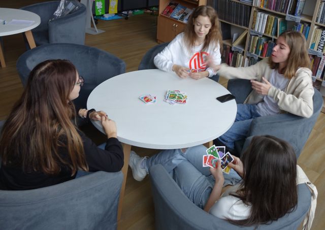 3 dziewczyny i chłopak grają w gry planszowe siedząc przy białym okrągłym stole