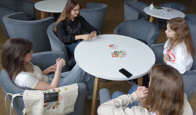 3 dziewczyny i chłopak grają w grę planszową przy białym okrągłym stole