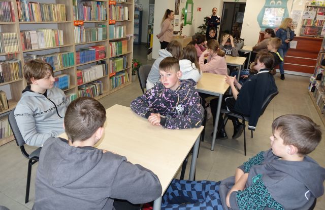 młodzież siedzi przy stolikach w pomieszczeniu bibliotecznym